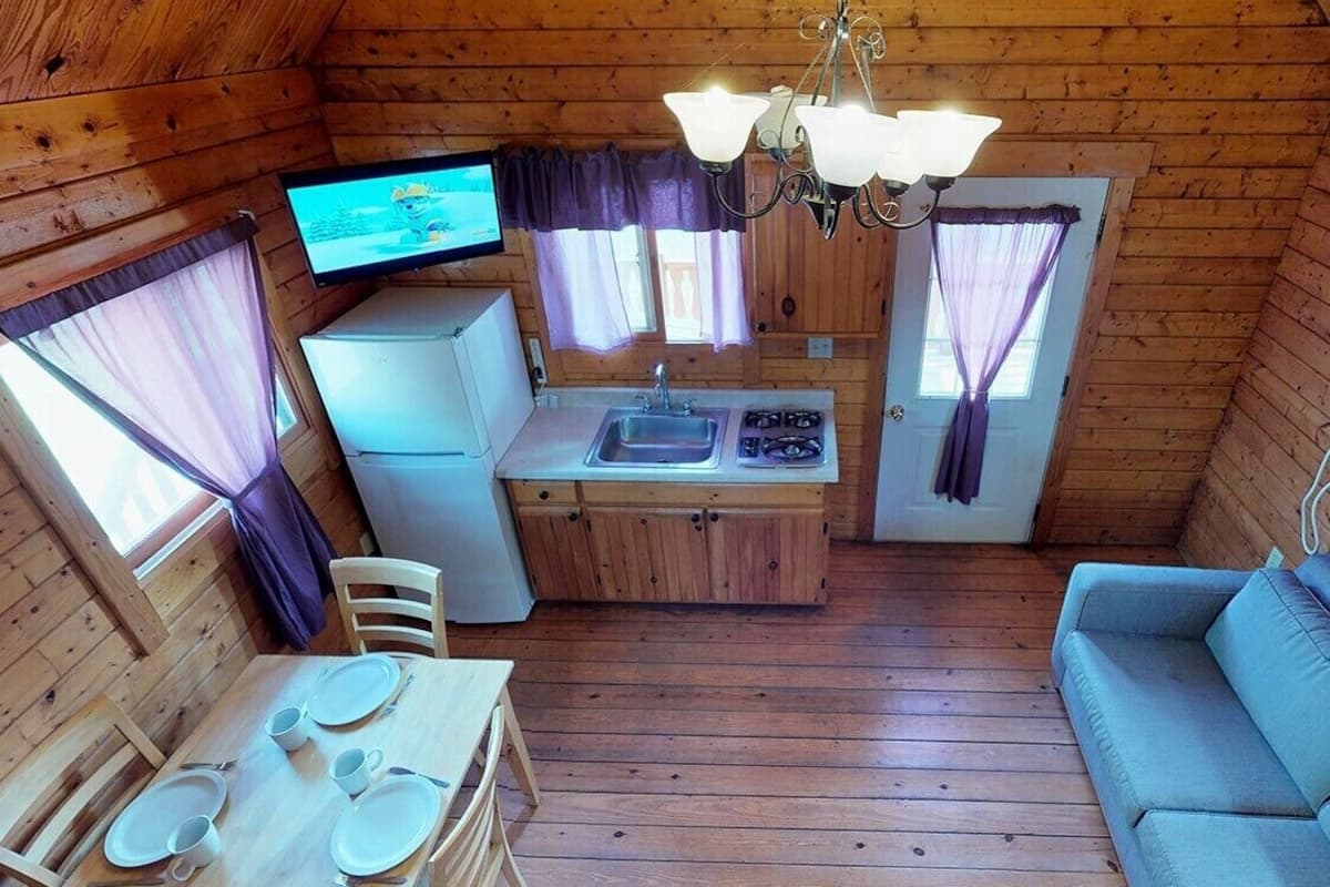 A compact wooden cabin with a kitchenette, dining table, and a sofa.