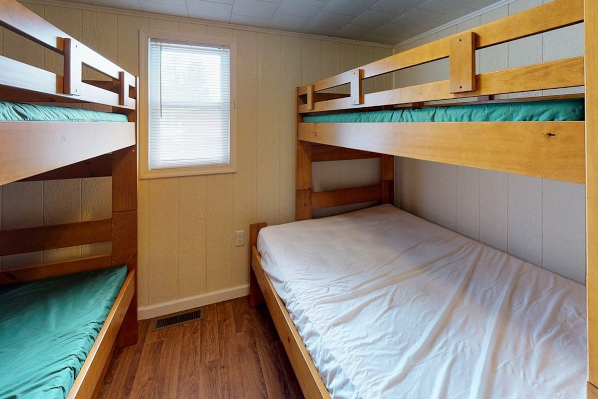 A dormitory room with bunk beds, a window, and wooden flooring.