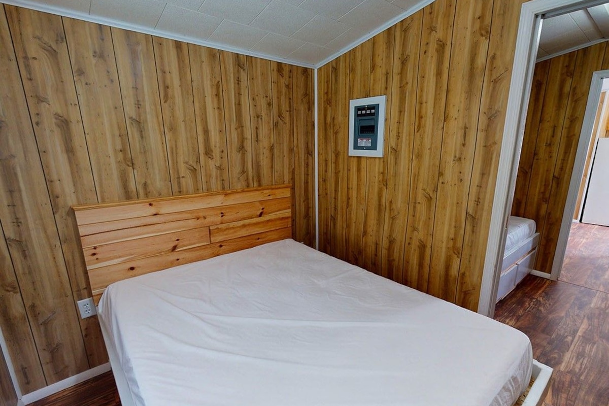 A bedroom with a wooden headboard, a white mattress, and a wall-mounted control panel.