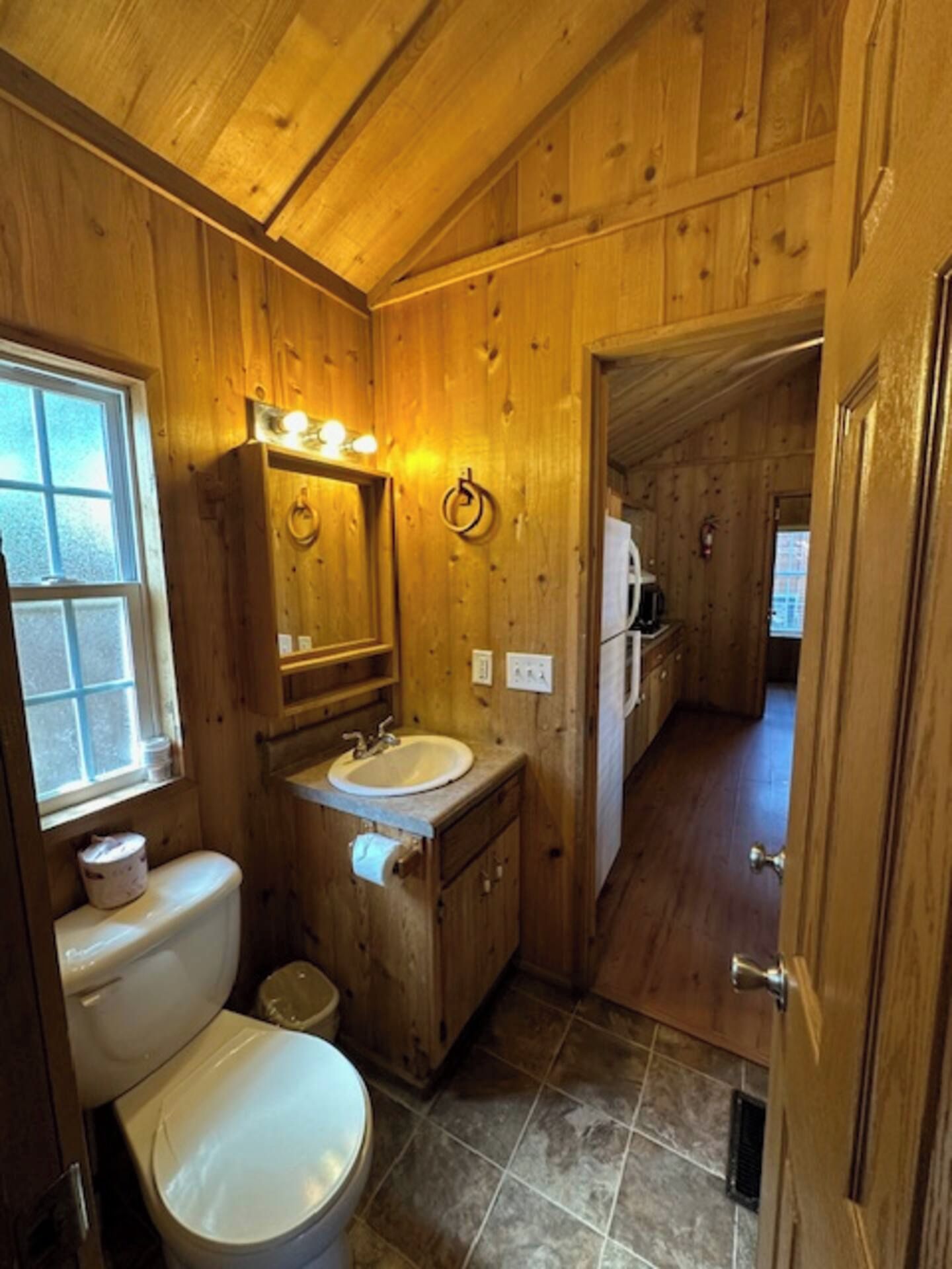A wooden bathroom with a toilet, sink, and mirror.