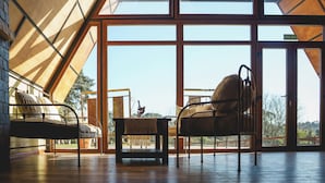A room with a bed, a chair, and a table. There is a large window with a view of the outdoors.