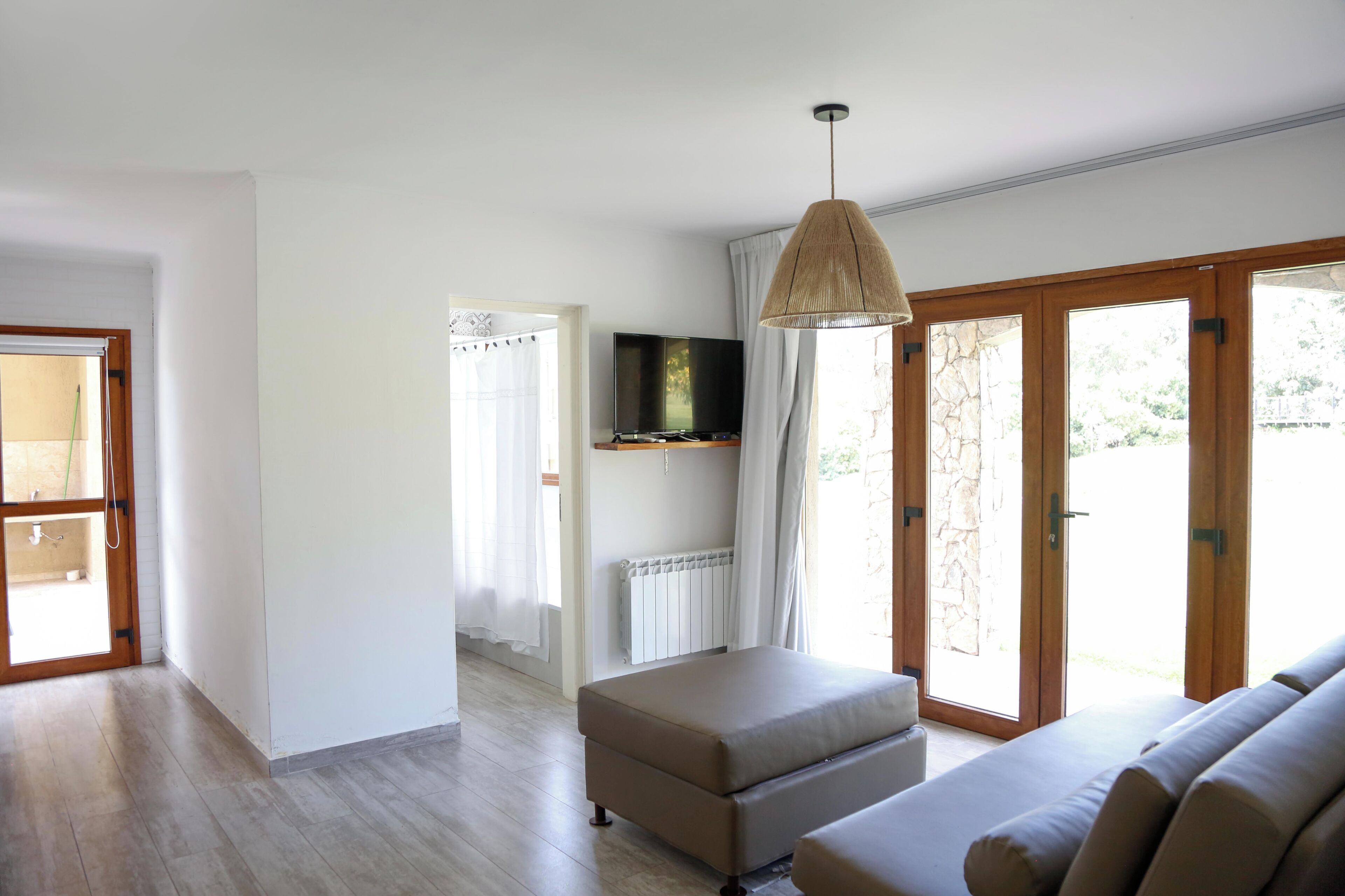 A room with a sofa, ottoman, television, and a hanging light fixture.