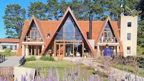 A modern building with a triangular roof, large windows, and a garden with purple flowers.