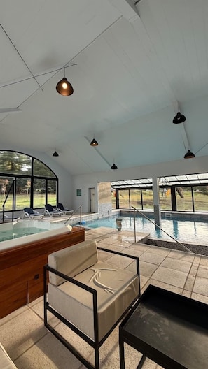 Un espace piscine avec des chaises longues, un jacuzzi et une vue sur l’extérieur.
