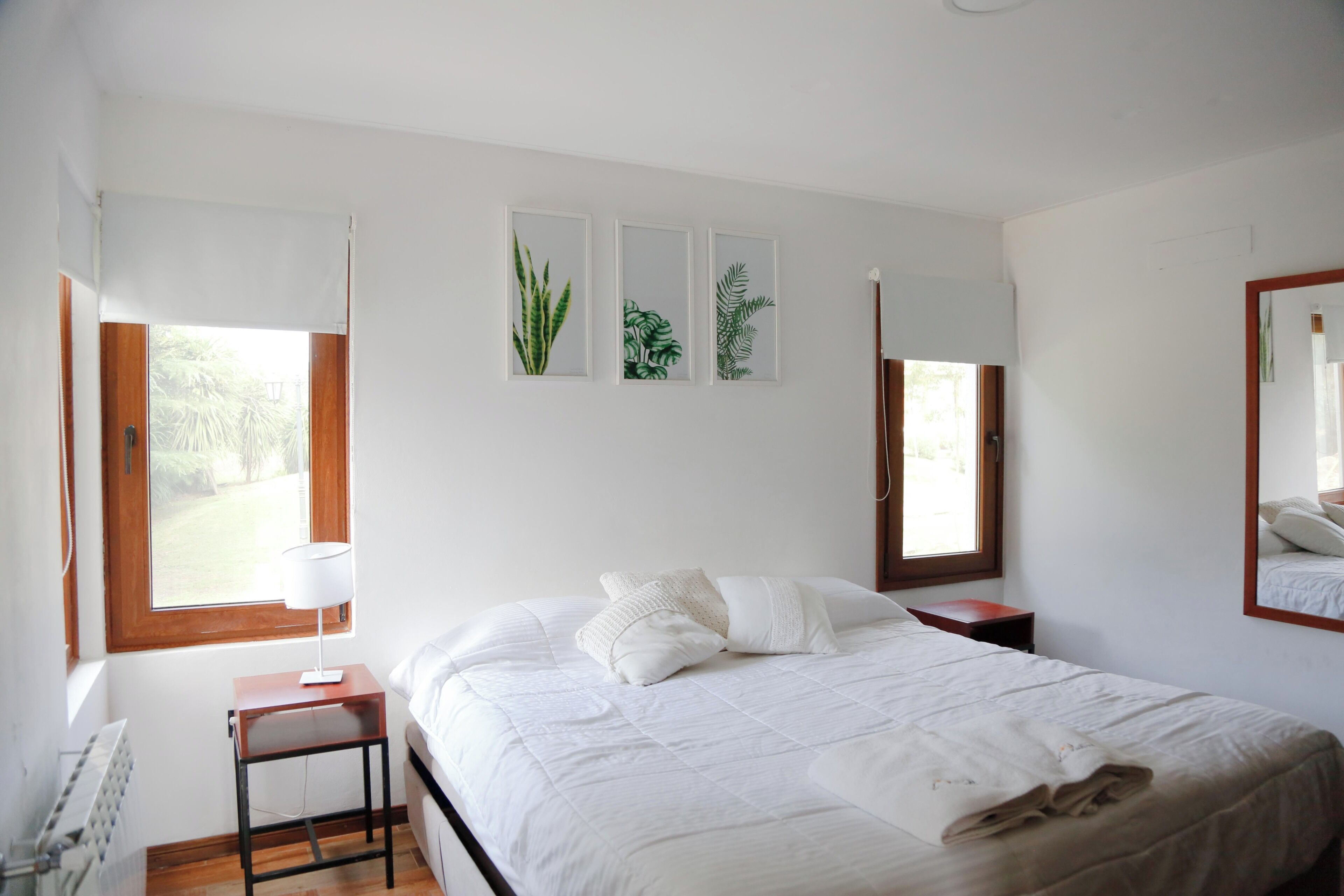 Un dormitorio con una cama, mesitas de noche, una lámpara e impresiones botánicas enmarcadas en la pared.