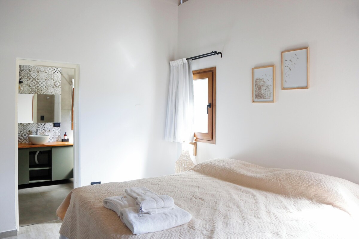 Un dormitorio con cama, un baño con lavamanos y un espejo.