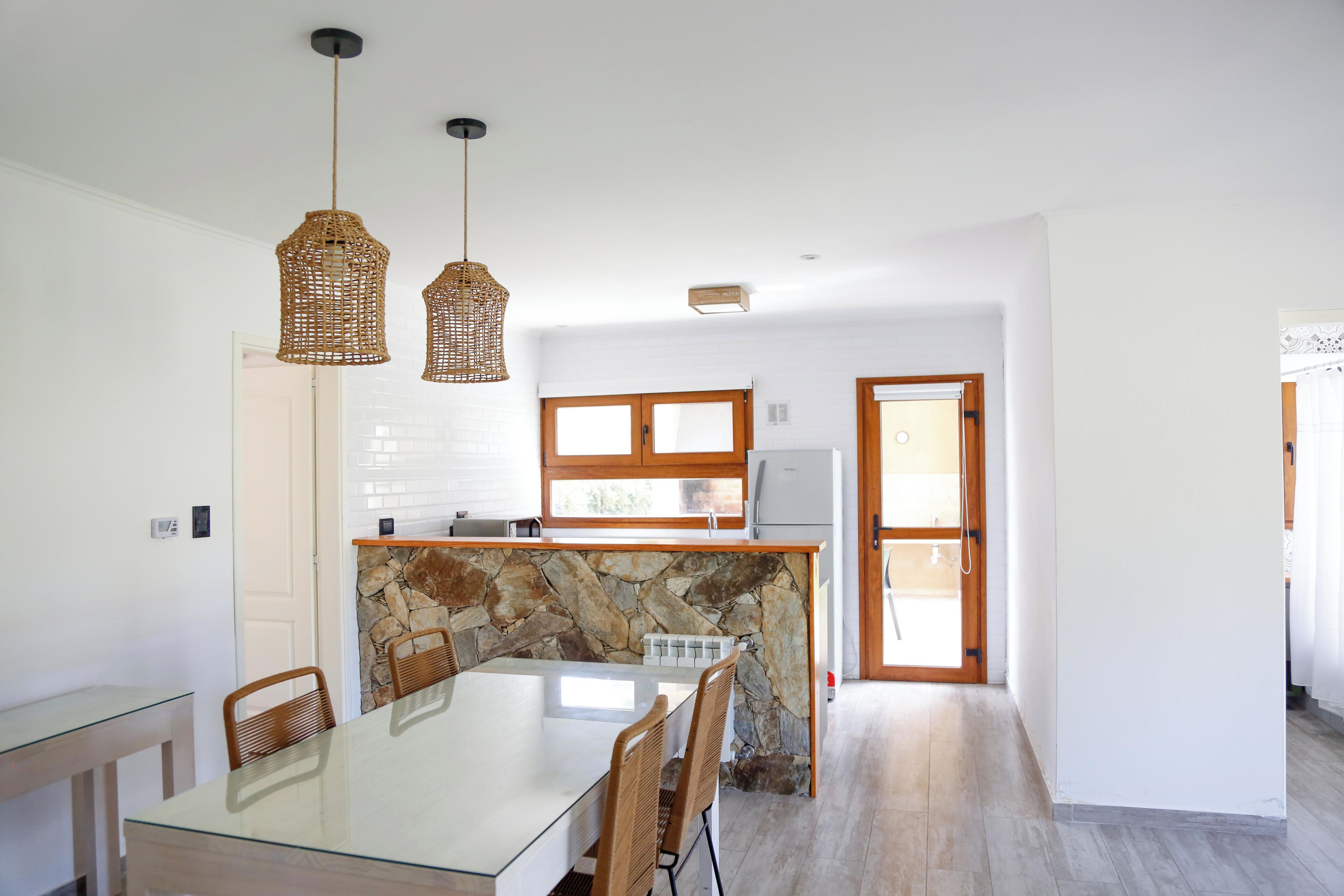 A modern kitchen with a stone backsplash, wooden cabinets, and a glass dining table.