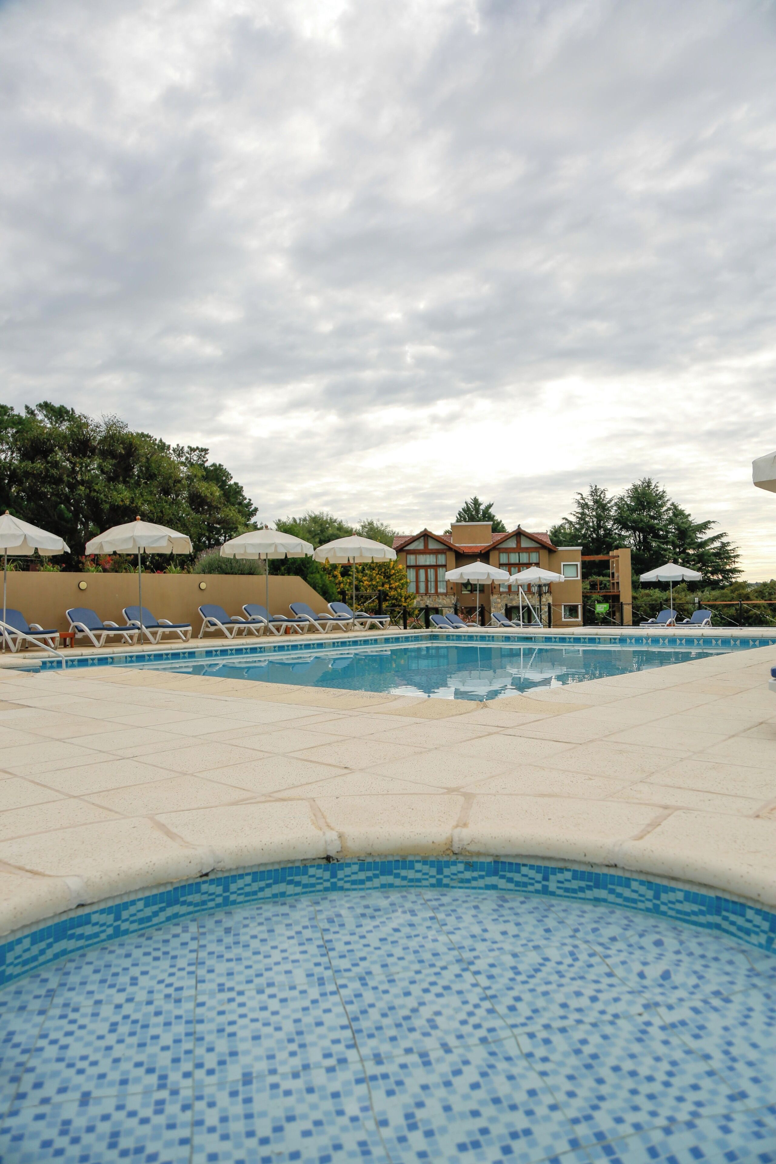 A swimming pool with lounge chairs and umbrellas, surrounded by buildings and trees.