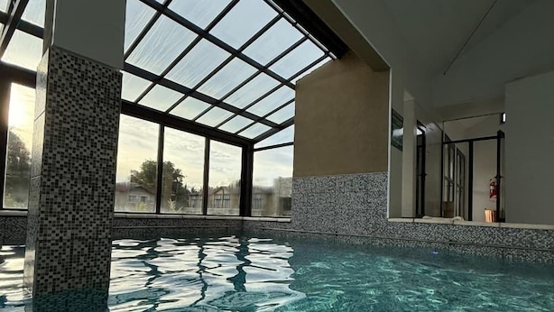 An indoor swimming pool with clear water, large windows, and tiled walls.