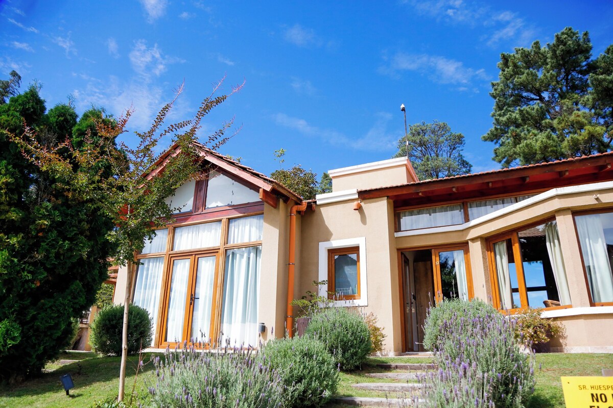 Una casa de dos pisos con jardín, un letrero y un cielo azul despejado.