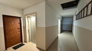 A hallway with a wooden door, a black doormat, and a ceiling vent.