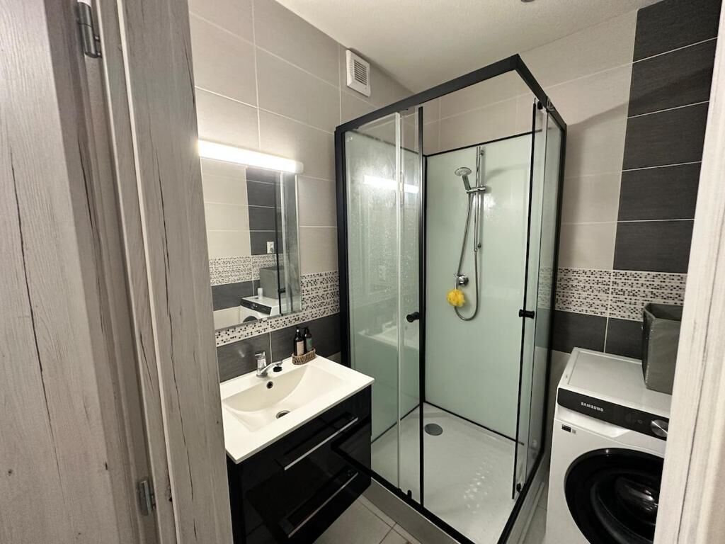 Een moderne badkamer met een douchecabine van glas, een wastafel met spiegel en een wasmachine.