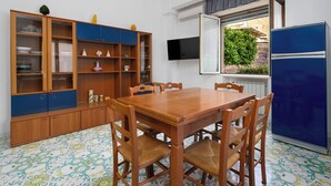 Een eetruimte met een houten tafel en stoelen, een blauwe kast met glazen deuren, en een aan de muur bevestigde televisie.