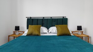Een bed met een blauwgroene spreidek, twee houten nachtkastjes, twee lampen en een hoofdbord met een horizontale stang.