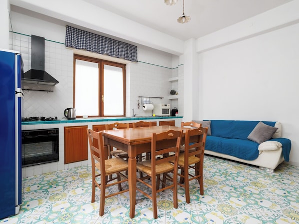 Eine kompakte Küche mit Esstisch, Stühlen, einem blauen Sofa und einem gemusterten Boden.