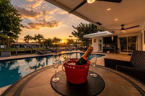 A poolside area with a bottle of champagne in a red bucket, two wine glasses, and a view of a sunset over a swimming pool. - Luxury Fort Lauderdale Waterfront Home • Heated Pool • Game Room •  Park (Fort Lauderdale)