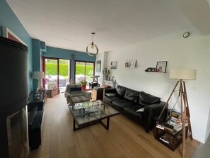 A living room with a glass coffee table, a black sofa, a lamp, and a bookshelf. - Le Minihic sur Rance - Charming house with its cat Platon between land and sea (Le Minihic-sur-Rance)
