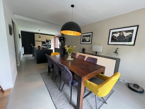 A modern dining area with a wooden table, purple and yellow chairs, a black pendant light, and a kitchen in the background. - Le Minihic sur Rance - Charming house with its cat Platon between land and sea (Le Minihic-sur-Rance)