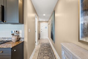 A hallway with a kitchen area on the left, a patterned rug, and a door at the end. - FREE Daily Golf! Reflections 406 Amazing Views, Heated Resort Pool & Hot Tub! (Panama City)