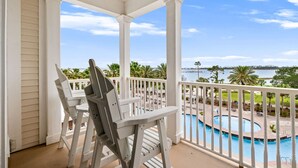 A covered balcony with white columns, a pool, and a view of a body of water. - FREE Daily Golf! Reflections 406 Amazing Views, Heated Resort Pool & Hot Tub! (Panama City)