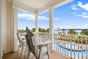 Ein überdachter Balkon mit weißen Säulen, ein Pool und Blick auf ein Gewässer.