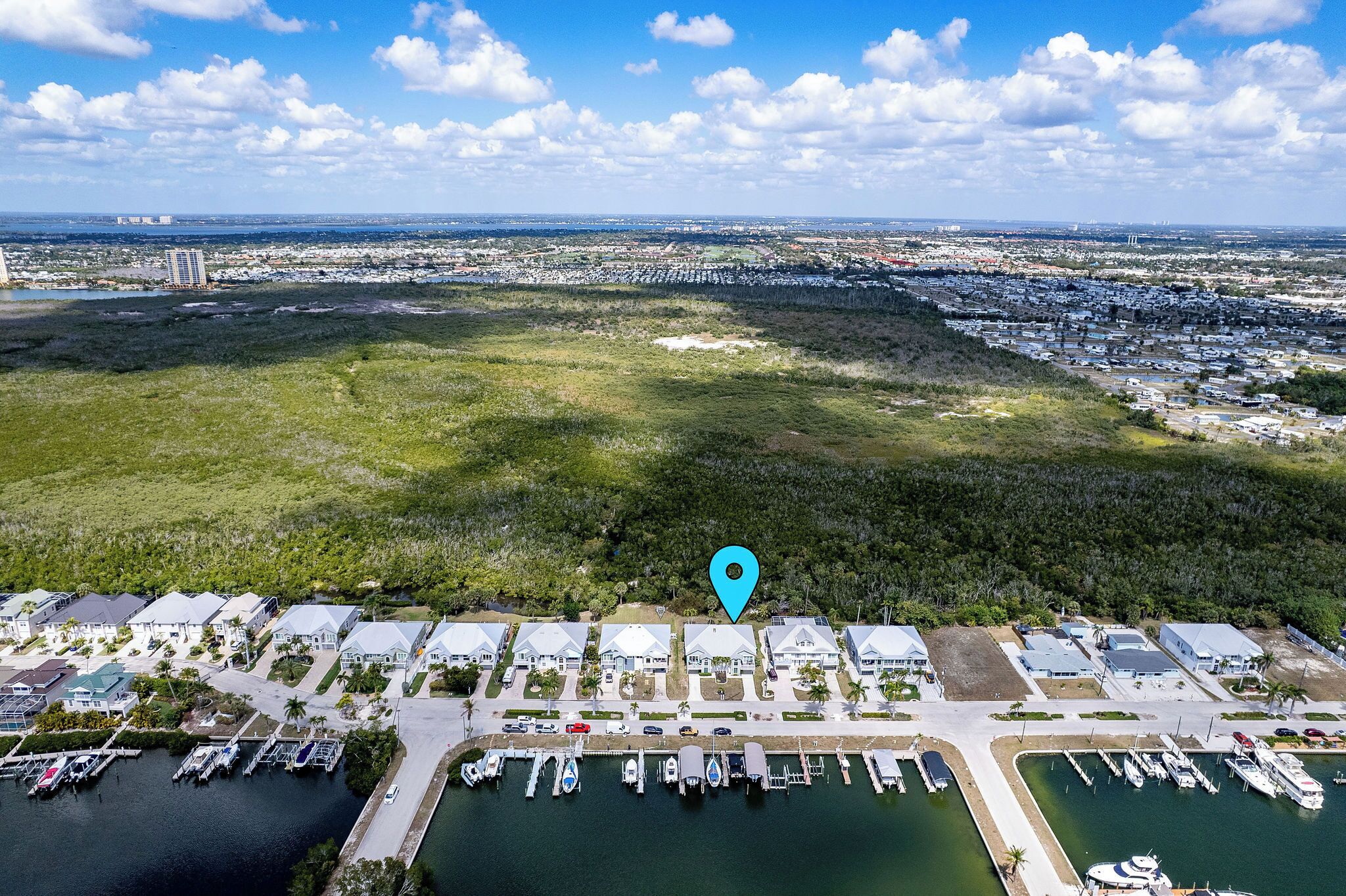 An aerial view of a marina with boats docked, surrounded by residential buildings and greenery.