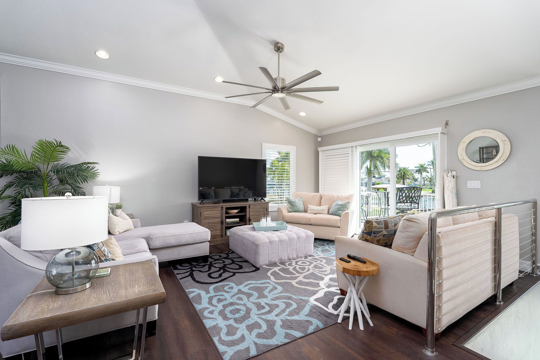 A living room with a ceiling fan, a flat-screen TV, a sofa, a coffee table, and a patterned rug.