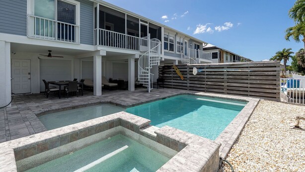 Un edificio de dos plantas con piscina, mobiliario exterior y un patio cubierto.