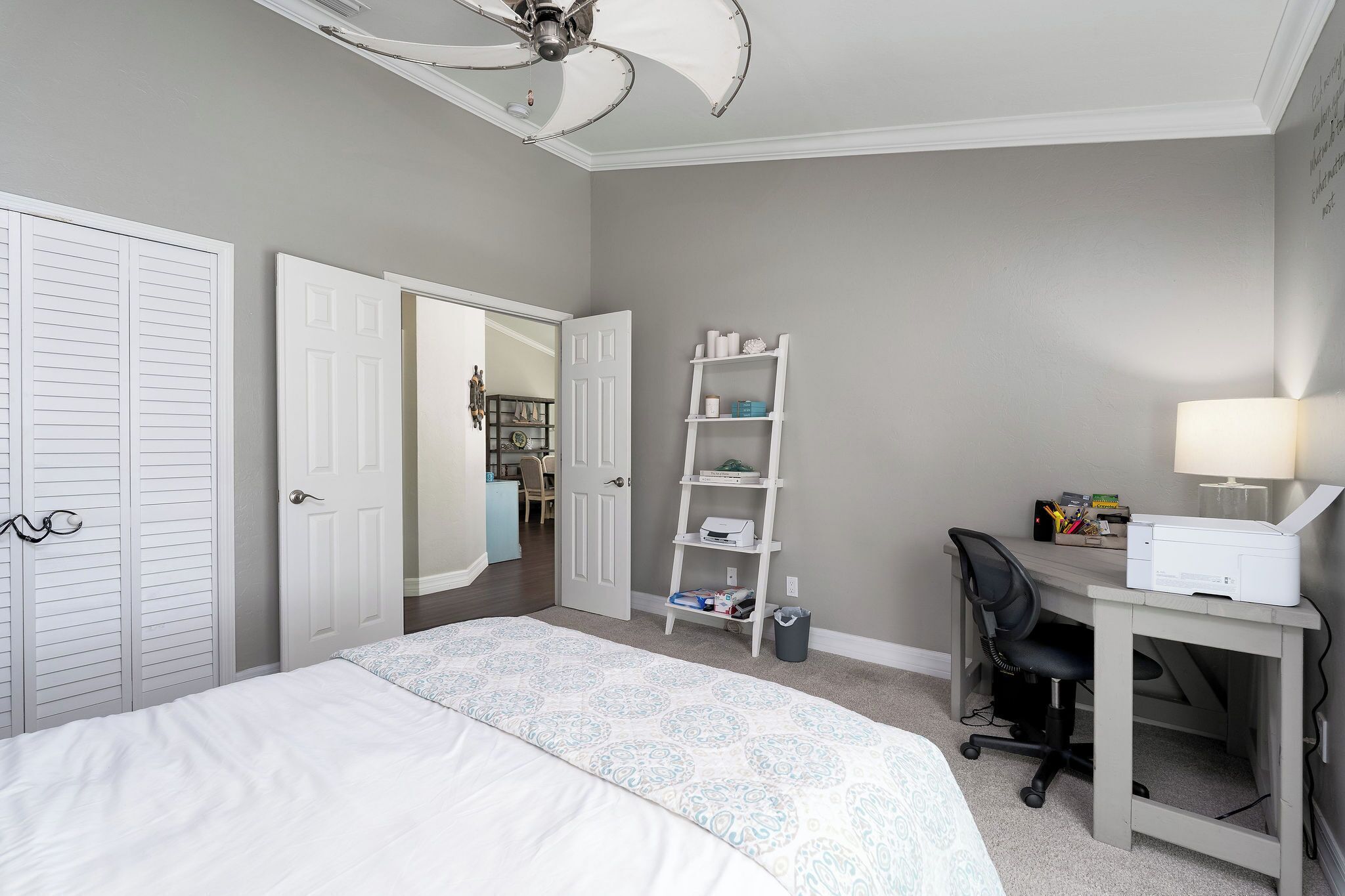 A bedroom with a bed, a desk with a chair, a ceiling fan, and a wardrobe.