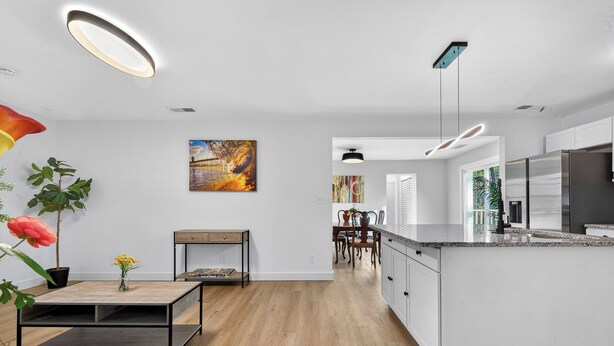 Eine moderne Küche mit einer zentralen Kochinsel, einem Essbereich mit Holztisch und einem Wohnbereich mit Sofa und Couchtisch.