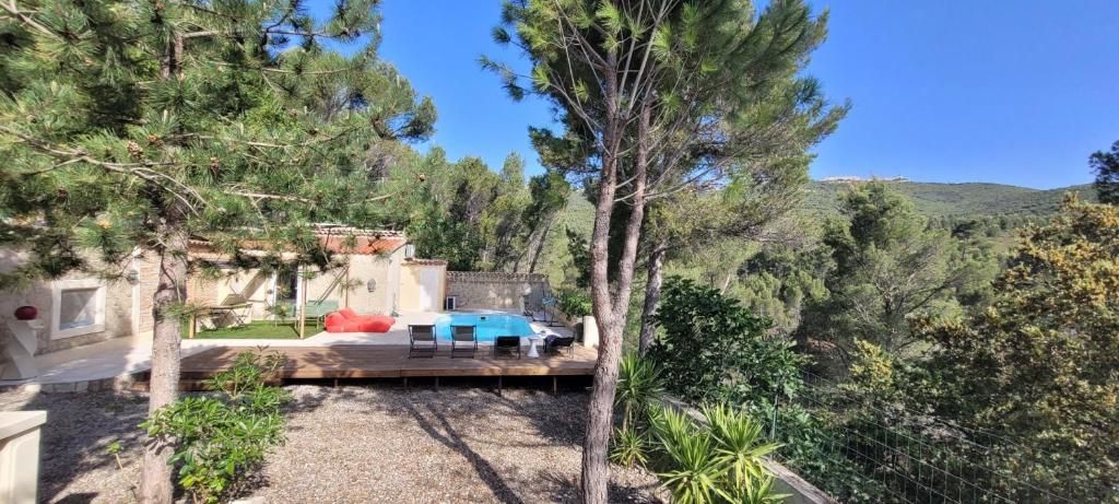 Un espace piscine doté de chaises longues, entouré d’arbres et offrant une vue sur un paysage vallonné.