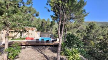Un espace piscine doté de chaises longues, entouré d’arbres et offrant une vue sur un paysage vallonné.