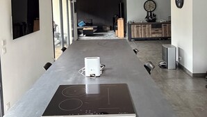 Eine moderne Küche mit integriertem Induktionskochfeld, einem Essbereich mit einem langen Tisch und einem Wohnbereich mit Sofa und Couchtisch.