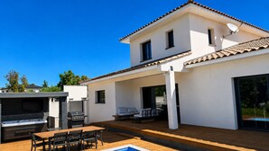 Ein zweigeschossiges Haus mit Swimmingpool, Sitzgelegenheiten im Freien und einer Grillgelegenheit.