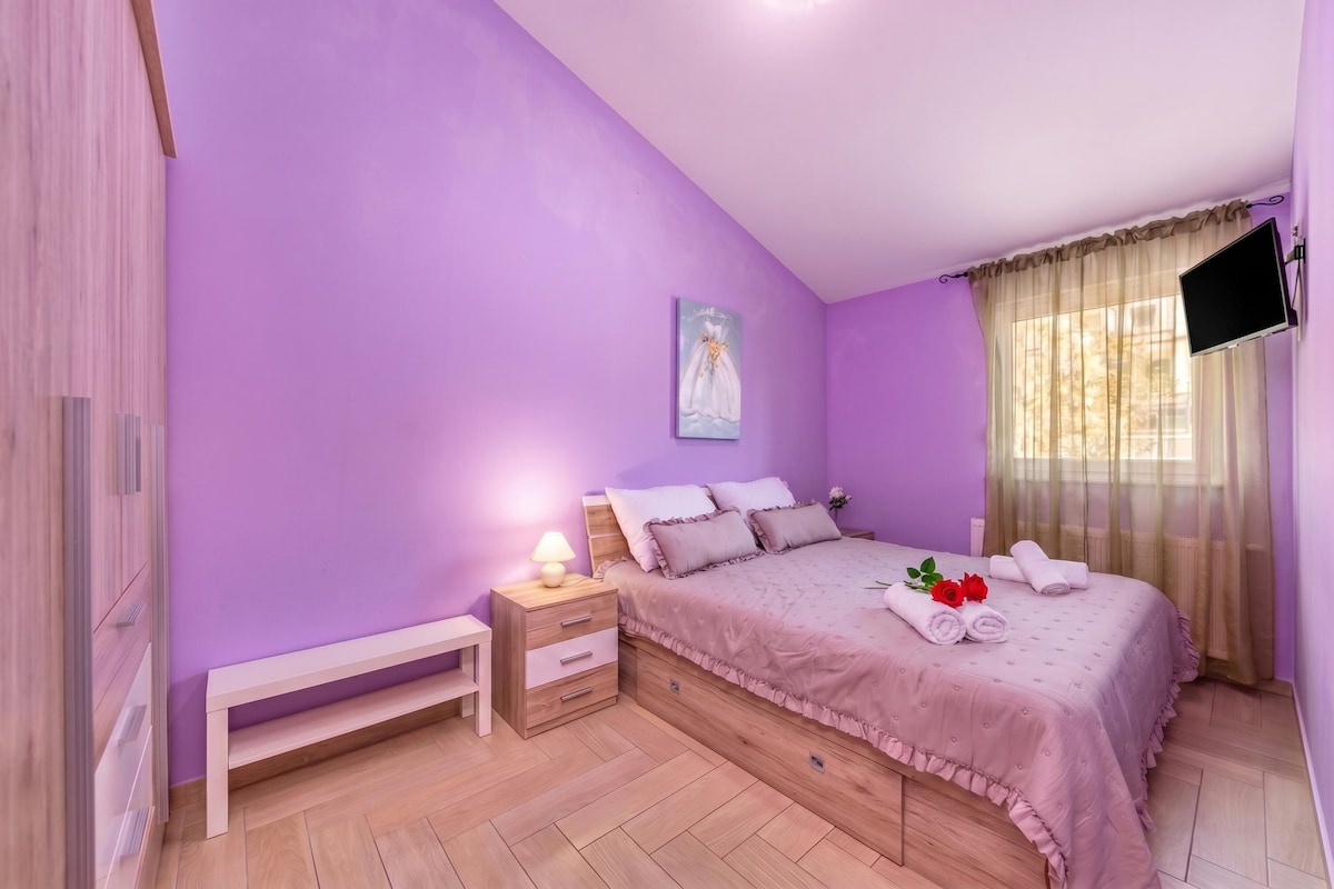 Een slaapkamer met een bed, nachtkastje, lamp en een schilderij aan de muur.