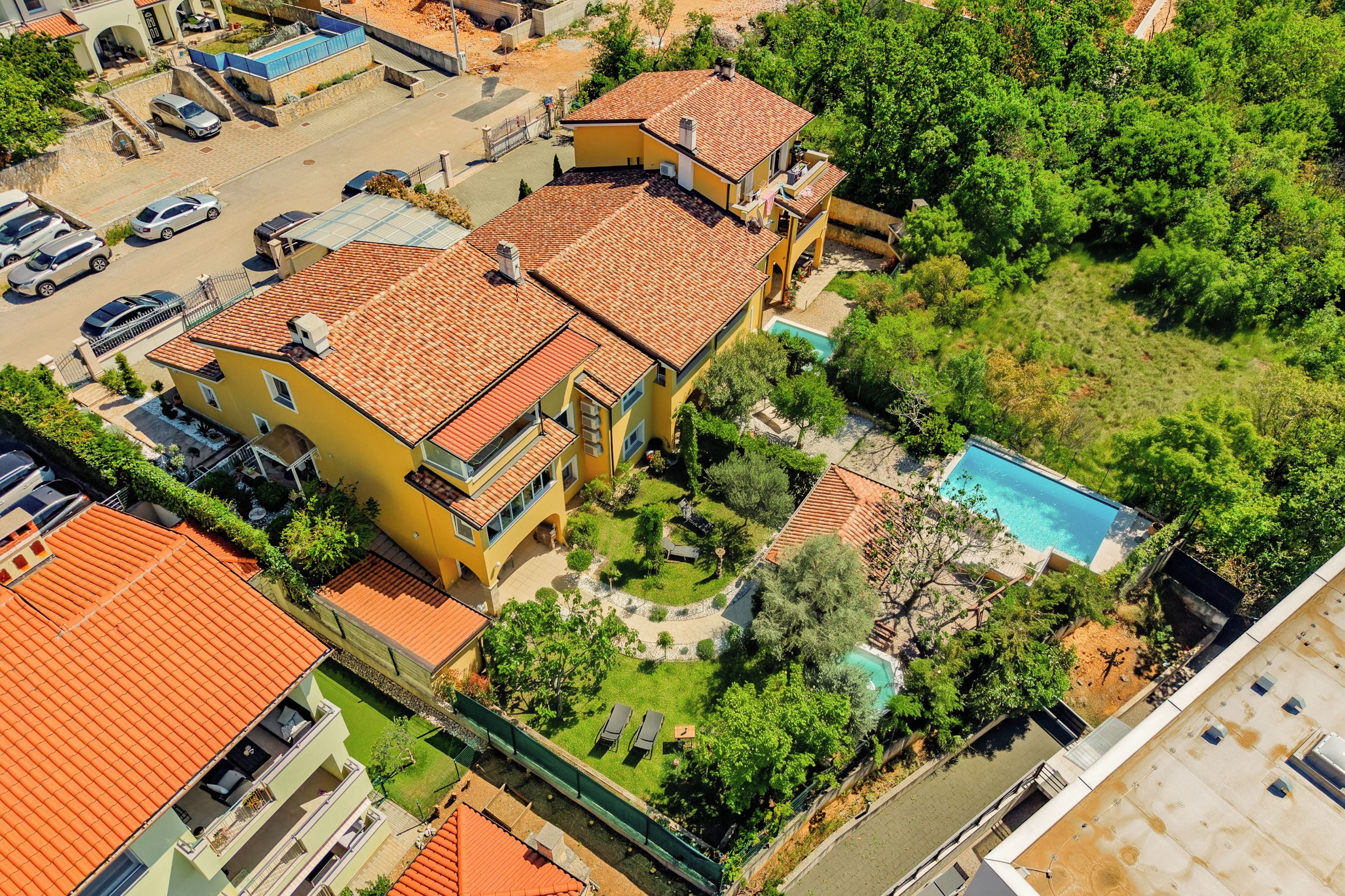 A multi-story residential building with a swimming pool, surrounded by greenery and parked cars.