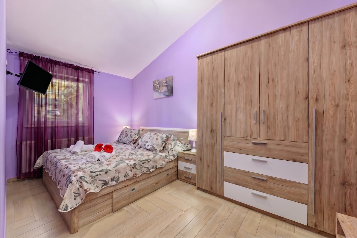 Een slaapkamer met een bed, een houten garderobe en een aan de muur bevestigde televisie.