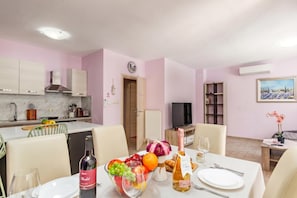 A dining area with a table set for two, a bottle of wine, and a bowl of fruit. - Pool and Garden Apartment Hortenzija (Kostrena)
