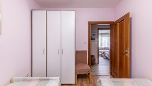A bedroom with two beds, a wardrobe, a chair, and a wooden door leading to another room. - Pool and Garden Apartment Hortenzija (Kostrena)