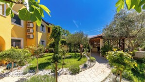 A courtyard with a stone pathway, greenery, and a building with multiple air conditioning units. - Pool and Garden Apartment Hortenzija (Kostrena)