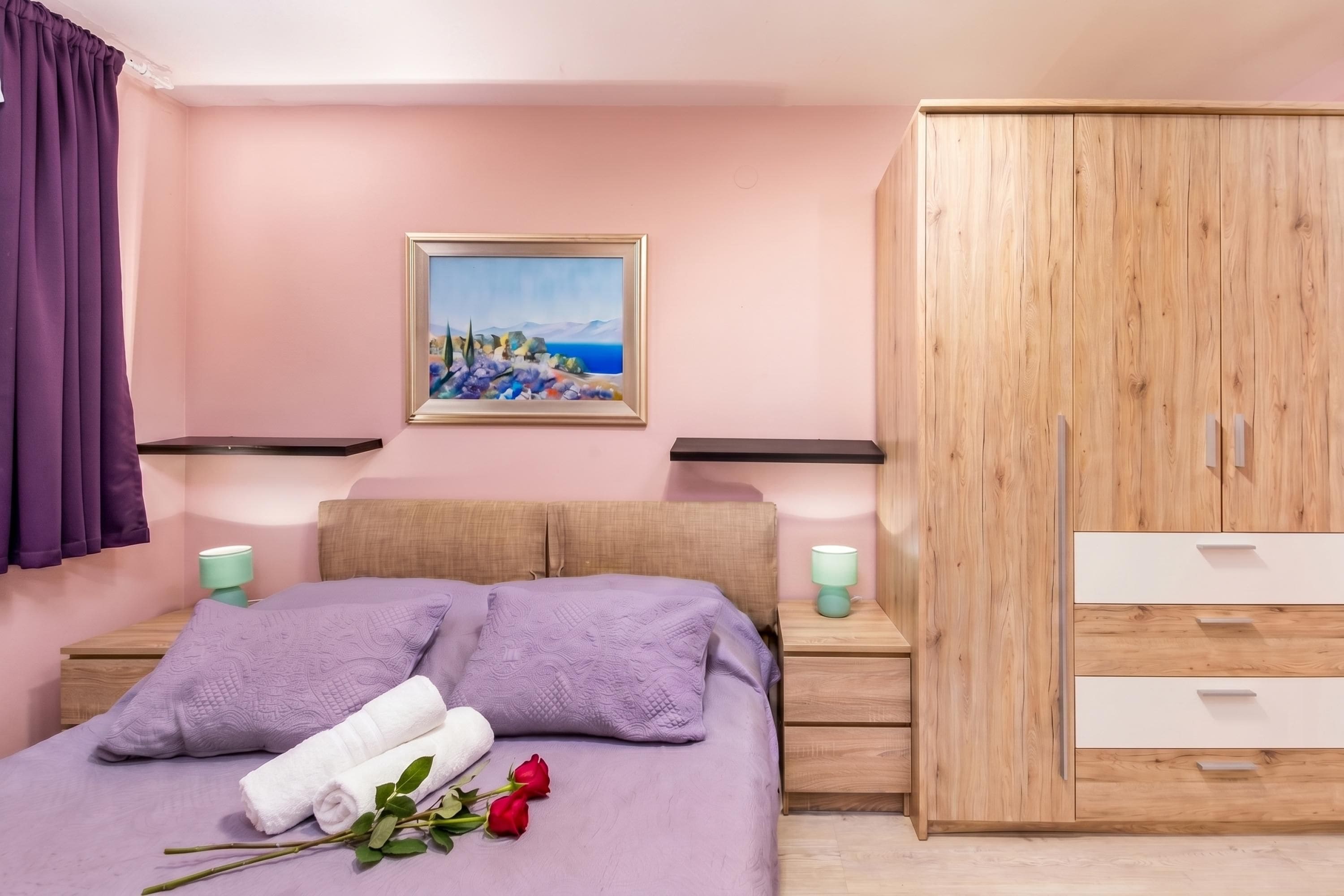 Een slaapkamer met een bed, een houten kledingkast, een nachtkastje met een lamp en een schilderij aan de muur.
