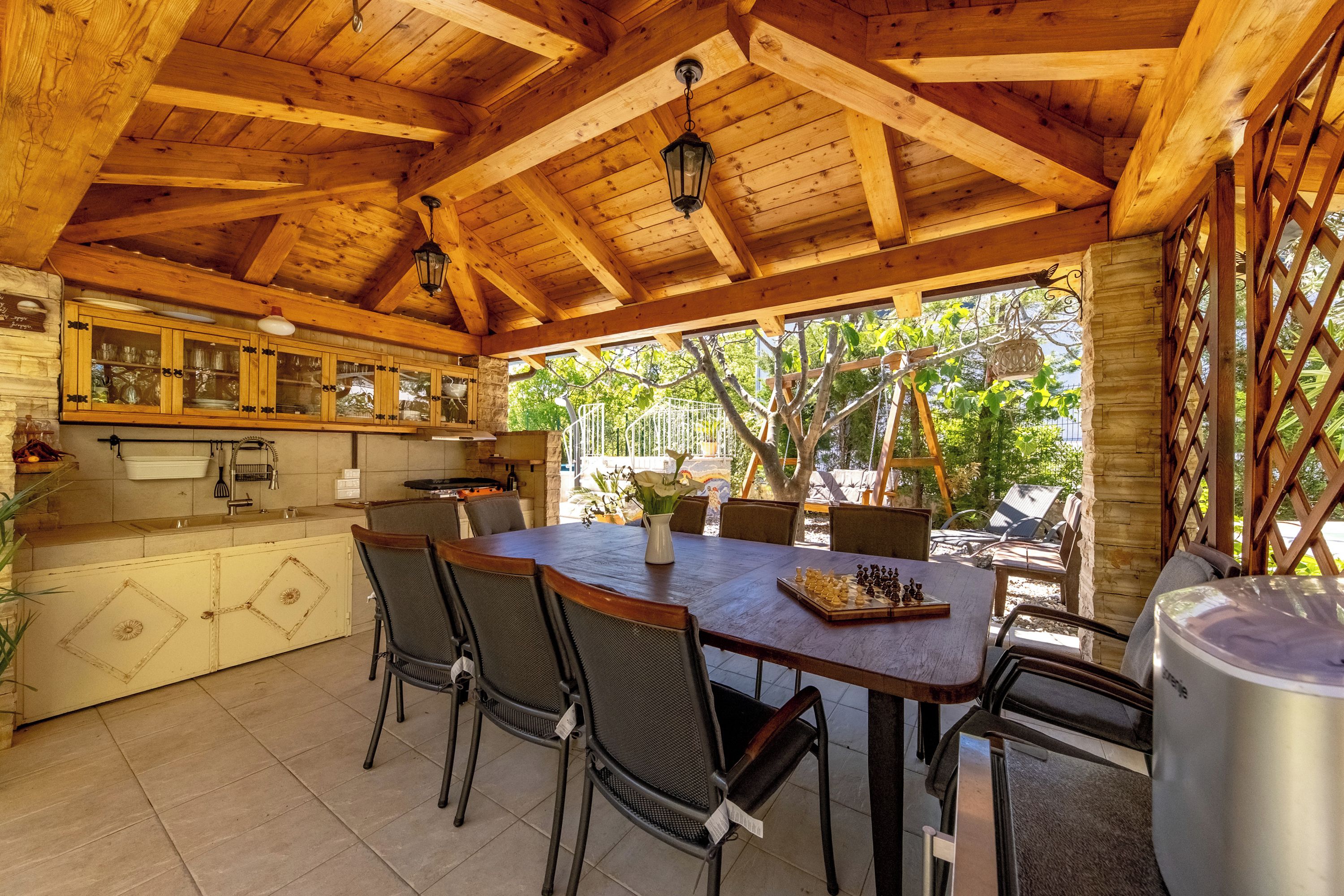 Une cuisine au plafond avec poutres apparentes, comprenant un coin repas avec une table, des chaises et une grande marmite.