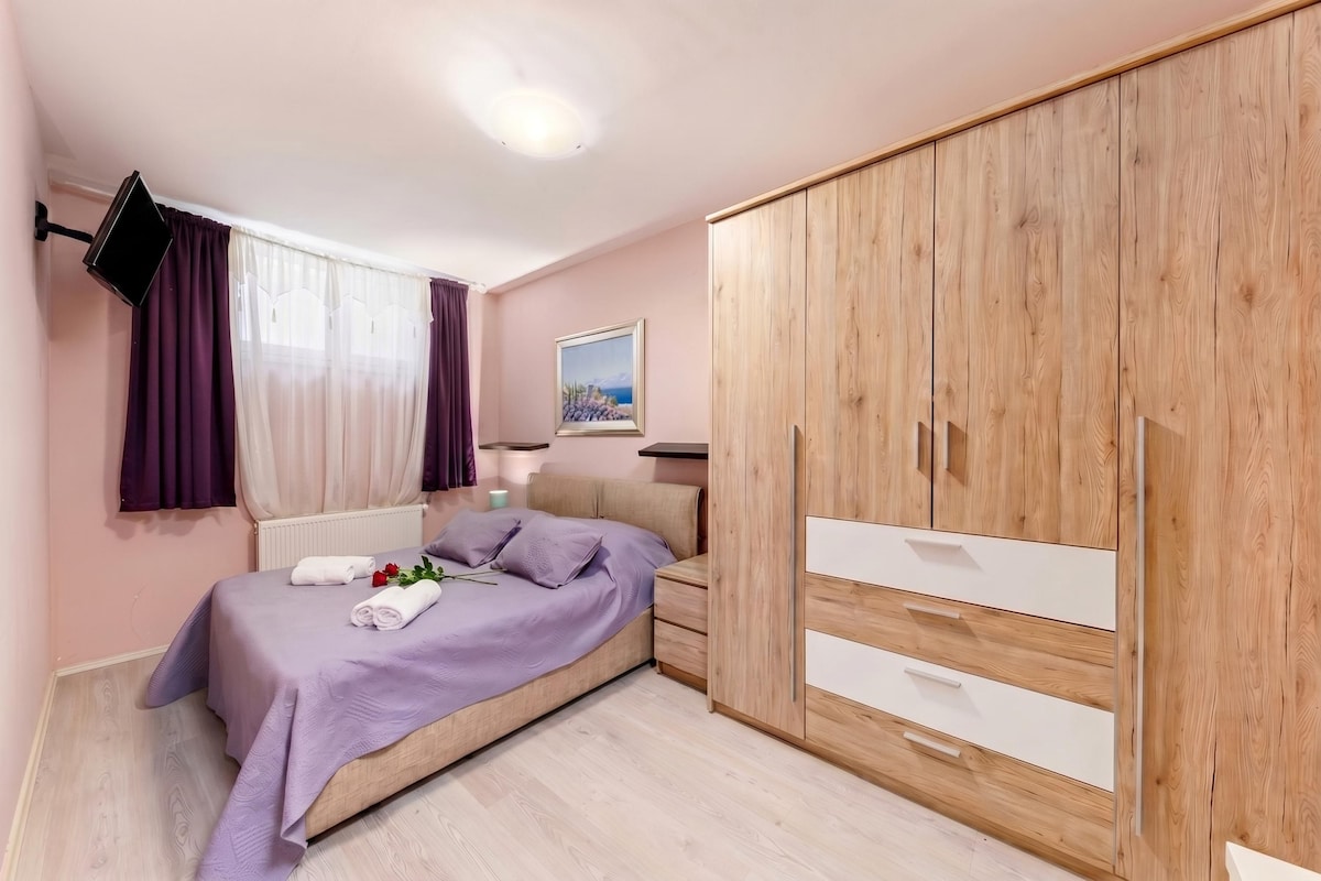 A bedroom with a bed, a wardrobe, a TV mounted on the wall, and a painting on the wall.