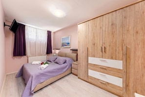 A bedroom with a bed, a wardrobe, a TV mounted on the wall, and a painting on the wall. - Pool and Garden Apartment Hortenzija (Kostrena)