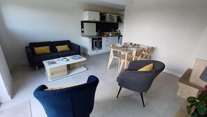 En kompakt opholdsstue med sofa, sofabord, spisebord med stole og et tekøkken.