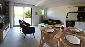 En moderne opholdsstue med spiseplads, sofa, tv ophængt på væggen og et køkken.