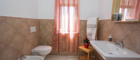 A bathroom with a bidet, toilet, sink, and shower curtain.