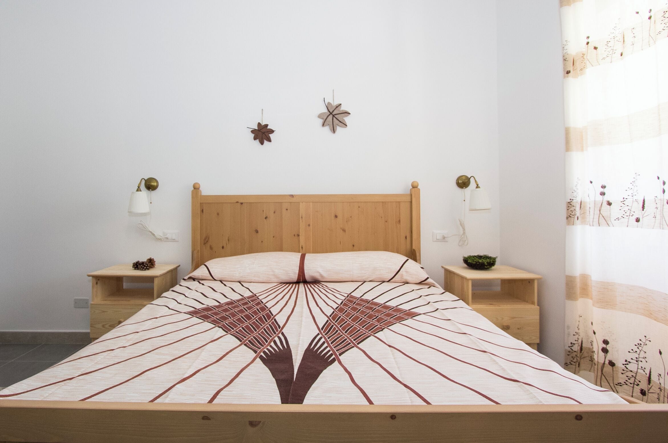 Een bed met een beddengoed met een geometrisch patroon, een houten hoofdbord, twee nachtkastjes met lampen en wanddecoraties.