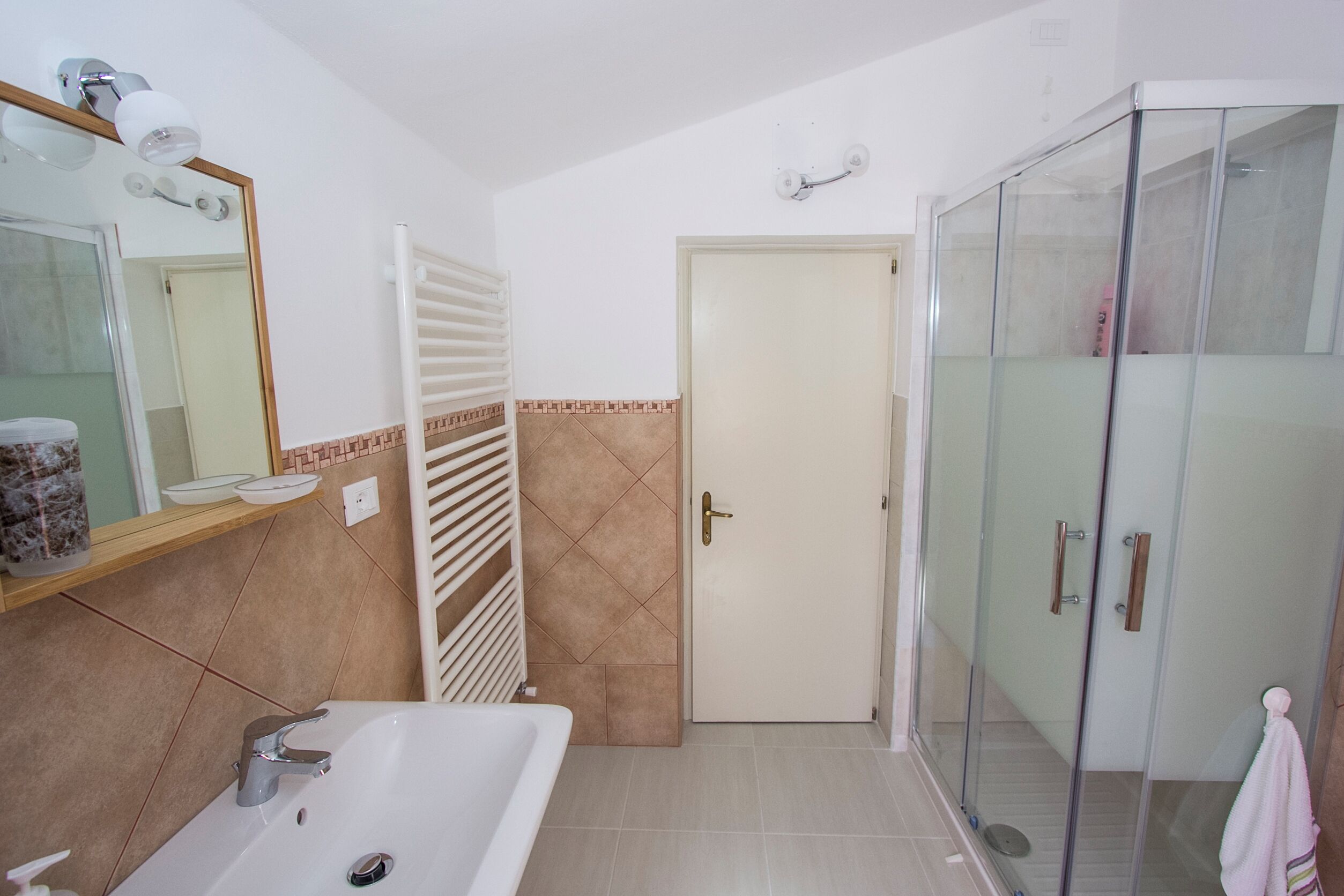 Un baño con bañera, cabina de ducha de vidrio, toallero y una puerta con una toalla colgada.