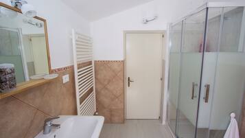 Un baño con bañera, cabina de ducha de vidrio, toallero y una puerta con una toalla colgada.